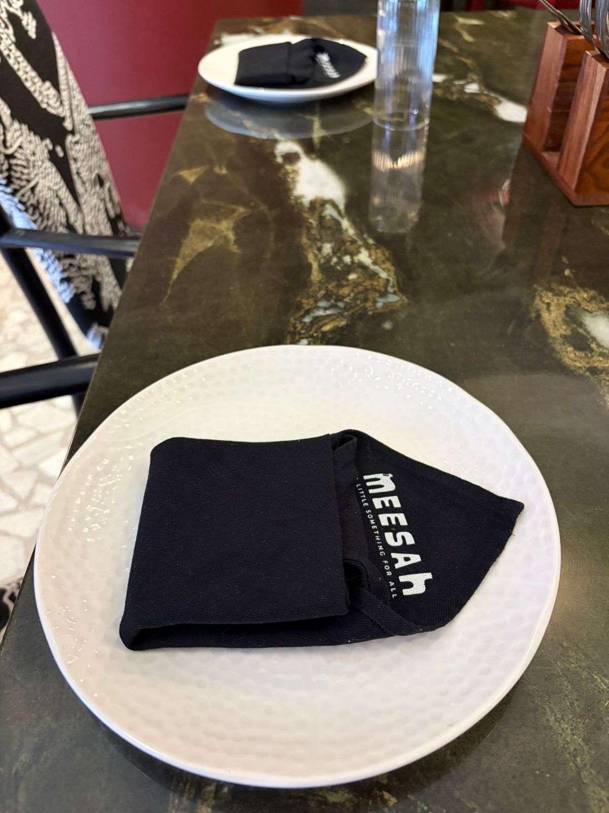 Meesah branded black napkin on white plate over dark marble