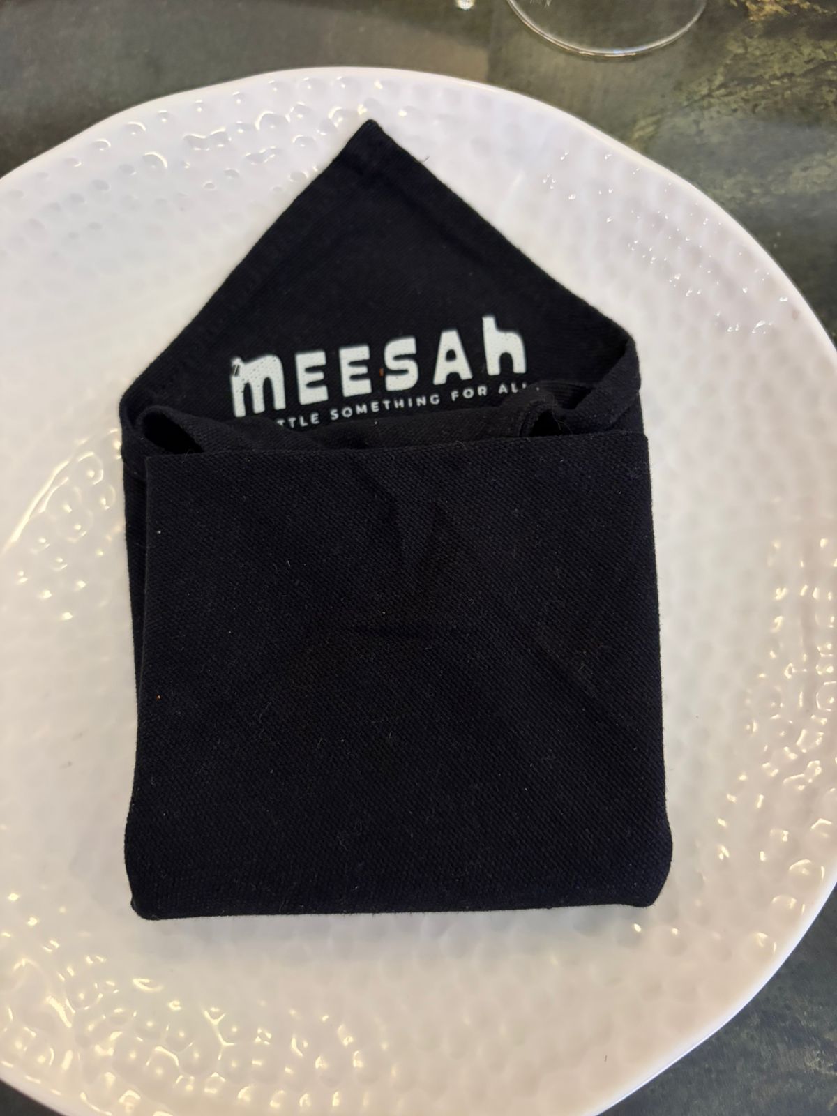 Close-up of Meesah branded black cloth napkin on textured plate